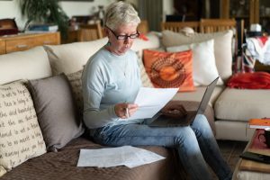 A grey-haired lady is looking at her paperwork and using her laptop to plan her financial budgets for her future